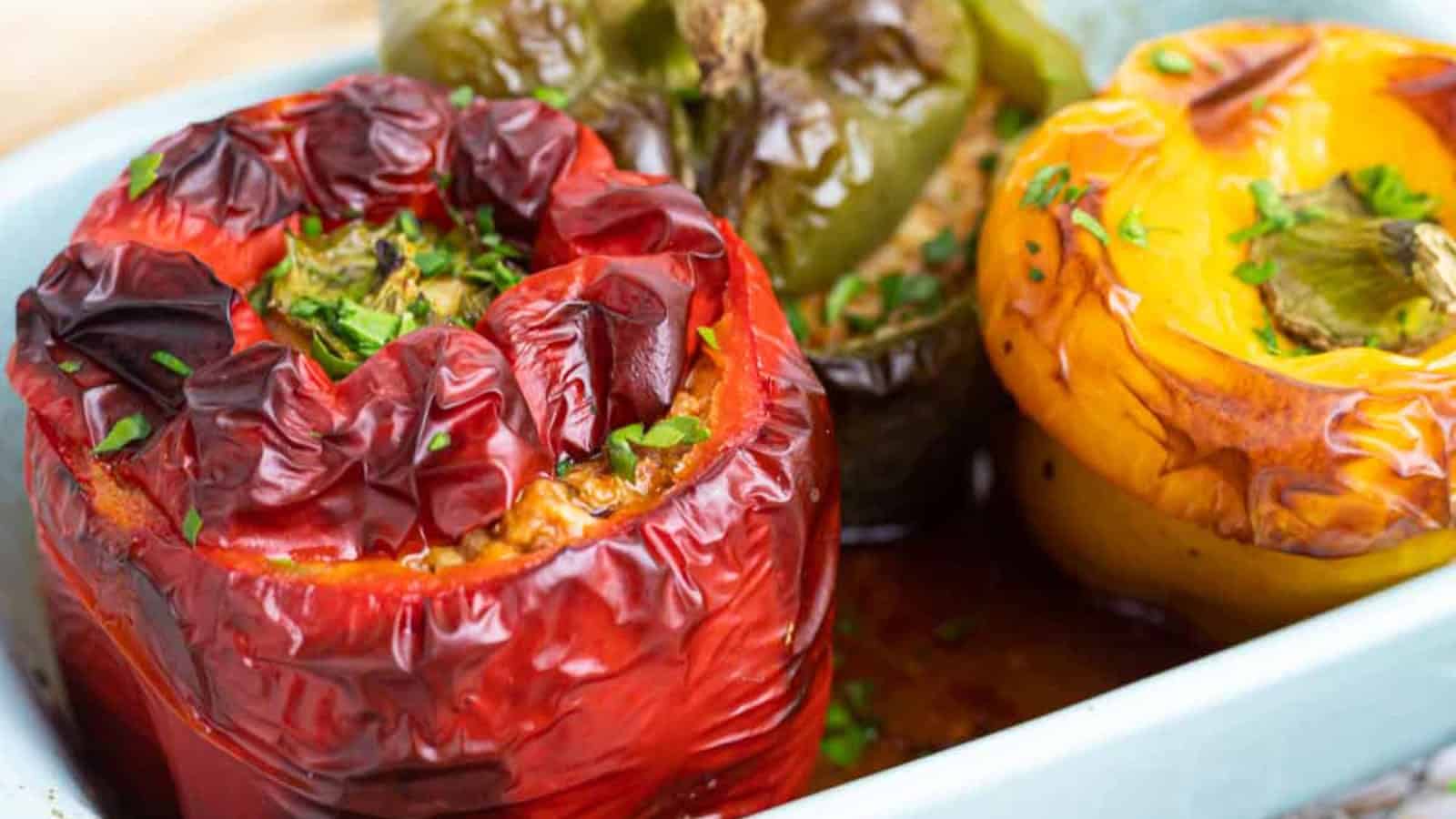 Three stuffed bell peppers—red, green, and yellow—in a baking dish, garnished with chopped herbs.