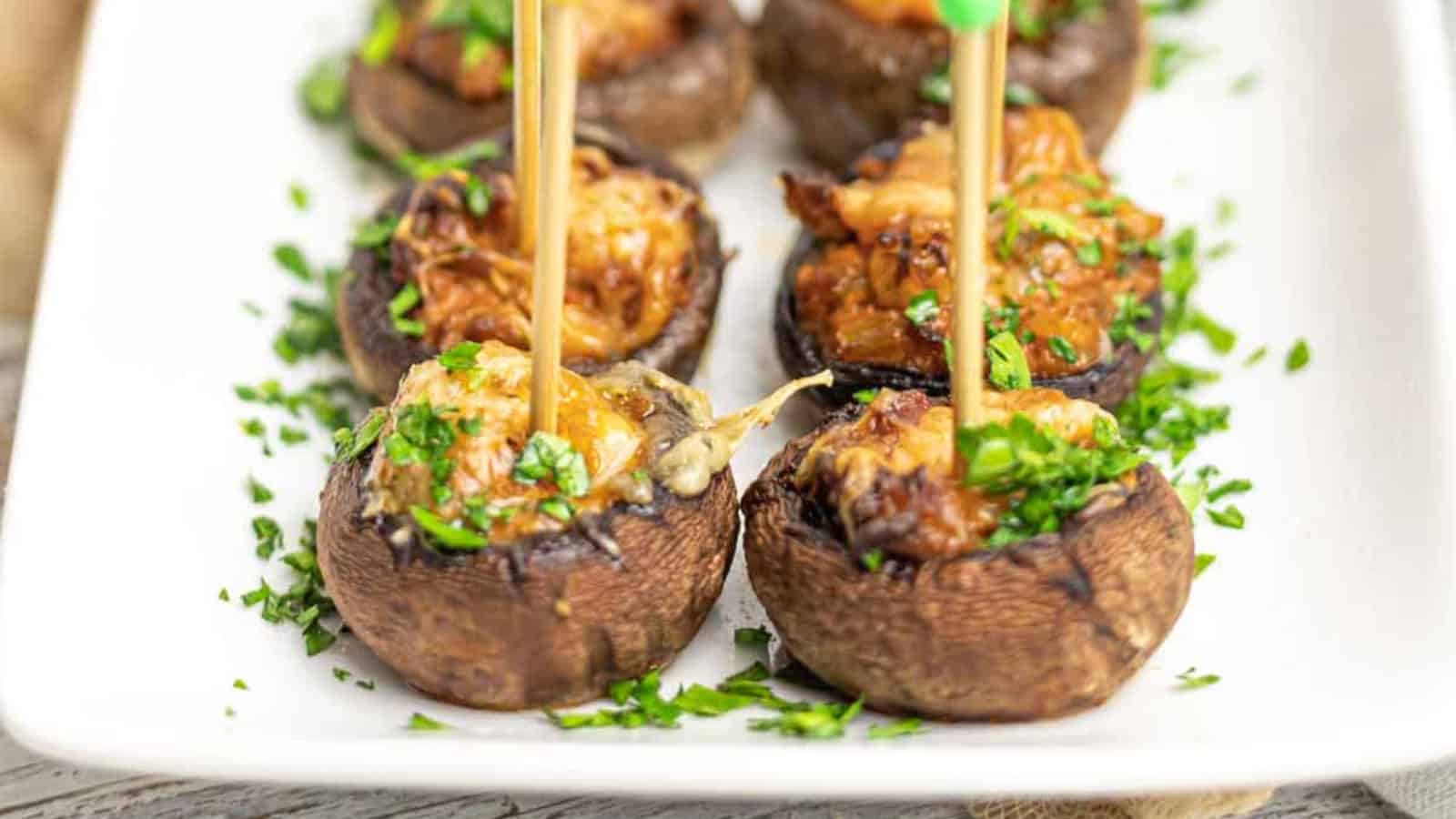 Stuffed mushrooms on a white plate, garnished with chopped parsley, each topped with a skewer.