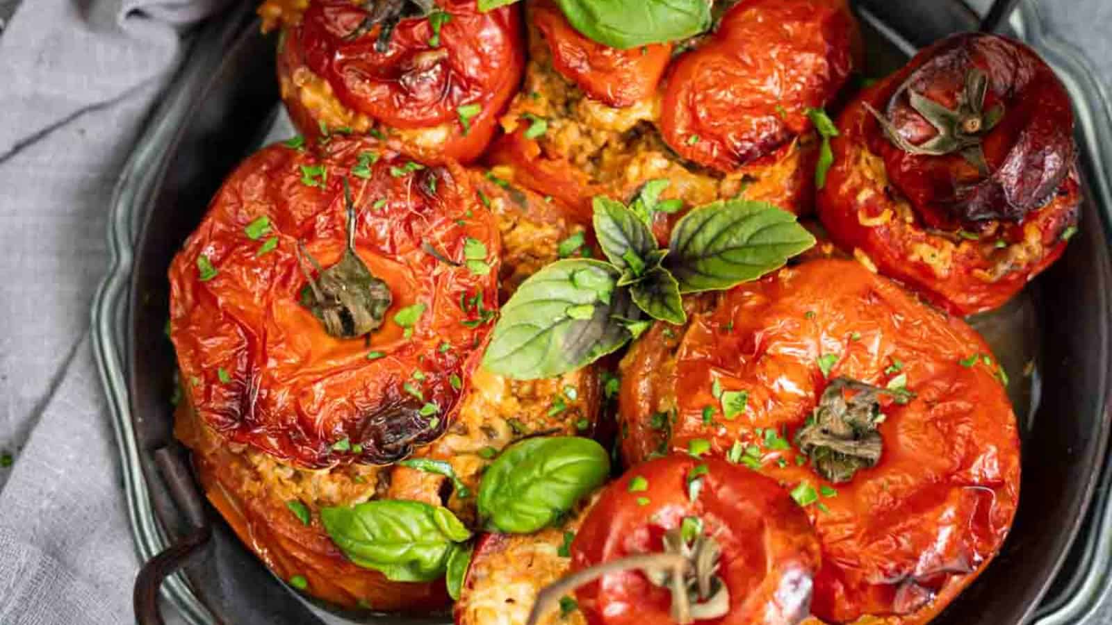 Baked stuffed tomatoes on a tray, garnished with fresh basil and parsley.