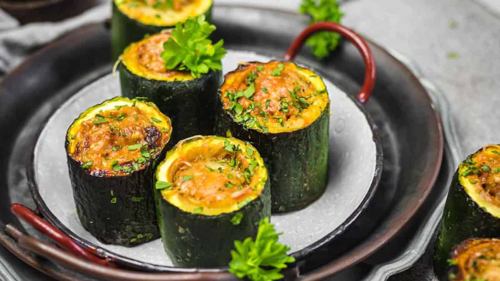 Round zucchini slices stuffed with a baked filling, garnished with parsley, served on a white plate with red-handled cookware.