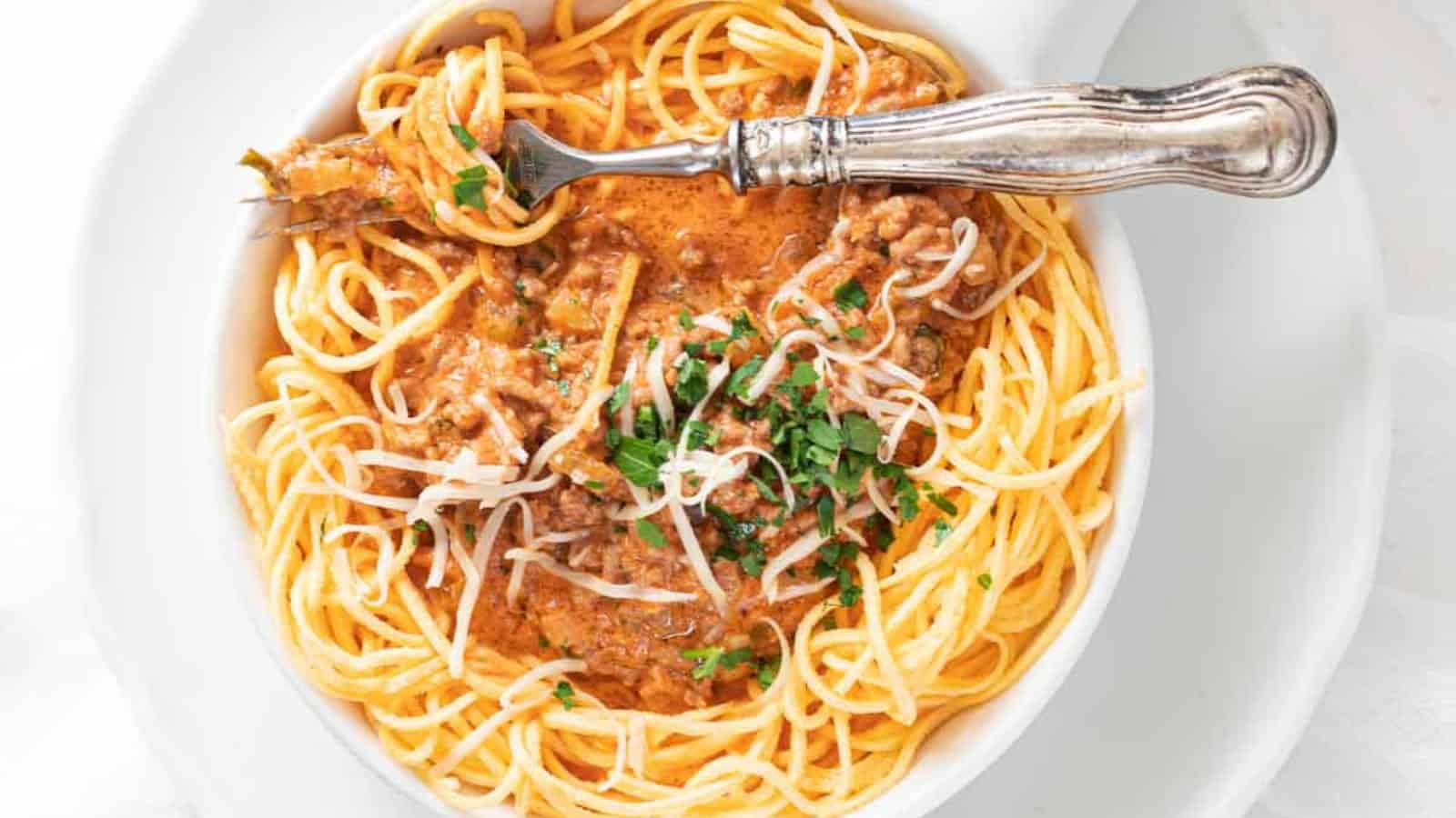 A bowl of spaghetti with meat sauce, topped with grated cheese and parsley, served with a silver fork.