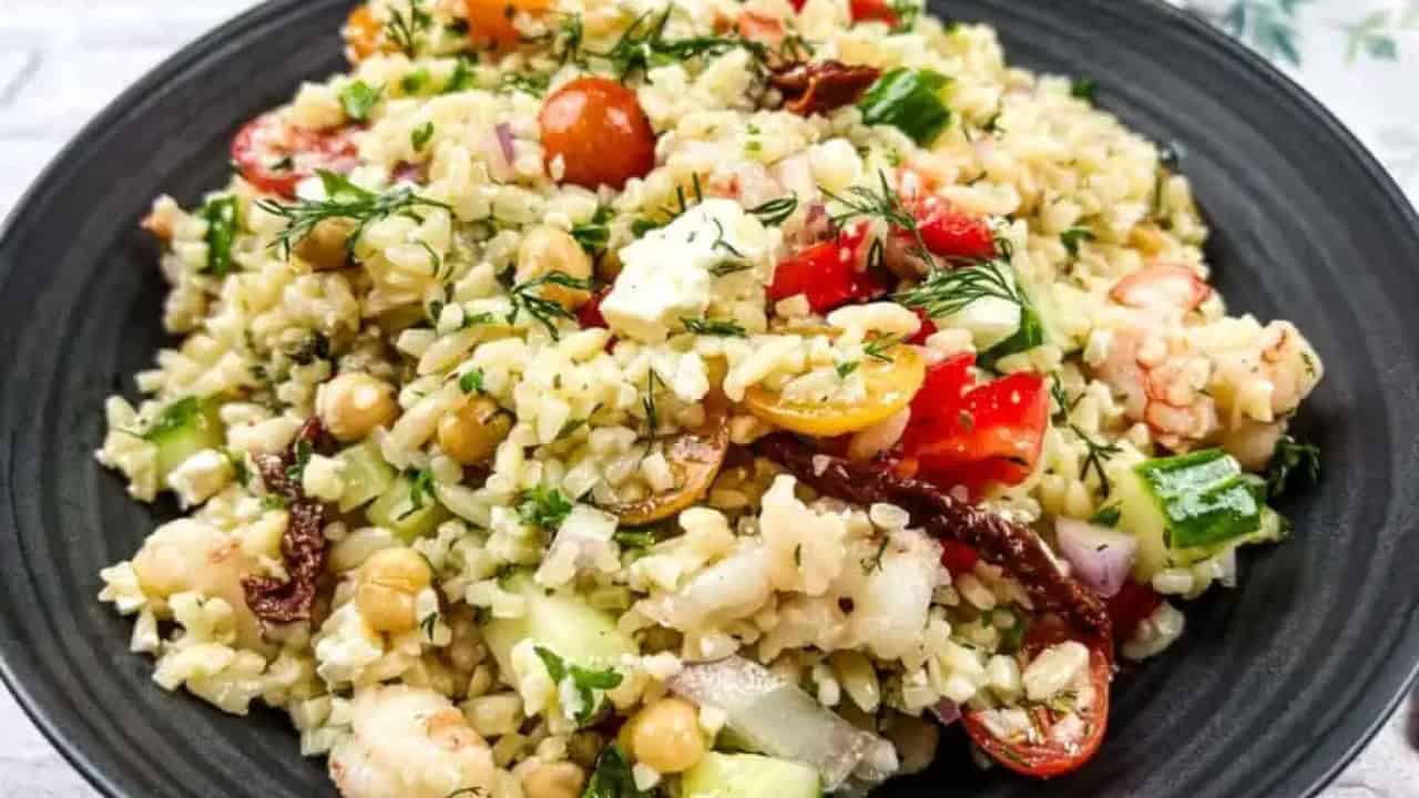 A plate of rice salad with cherry tomatoes, chickpeas, onions, cucumbers, herbs, and feta cheese.