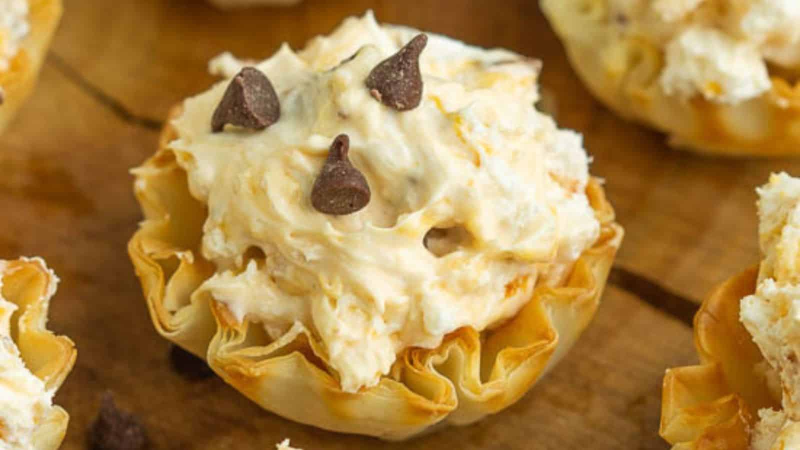A small pastry shell filled with creamy whipped topping and chocolate chips on a wooden surface.