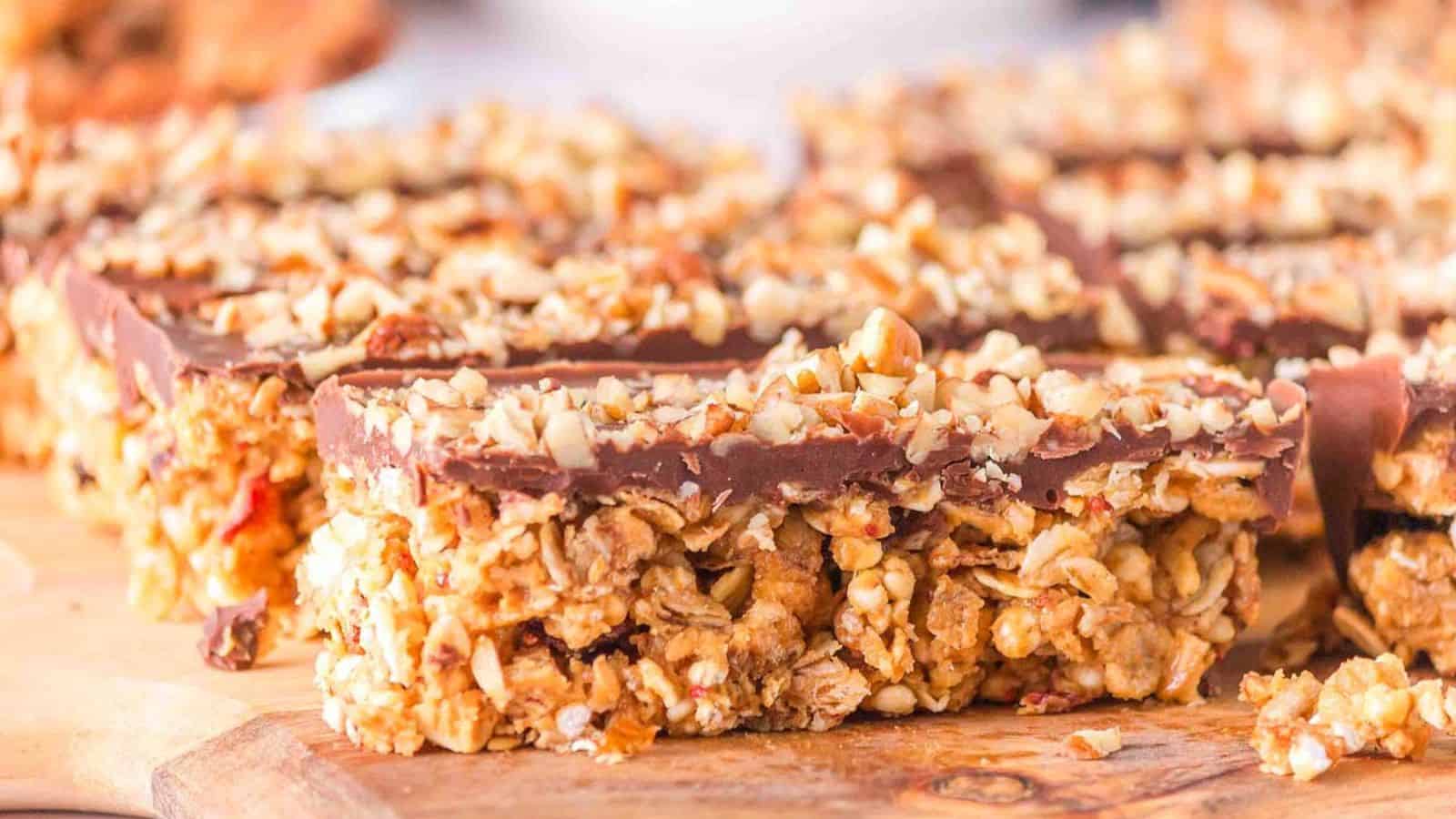 Granola bars topped with chocolate and nuts displayed on a wooden surface.