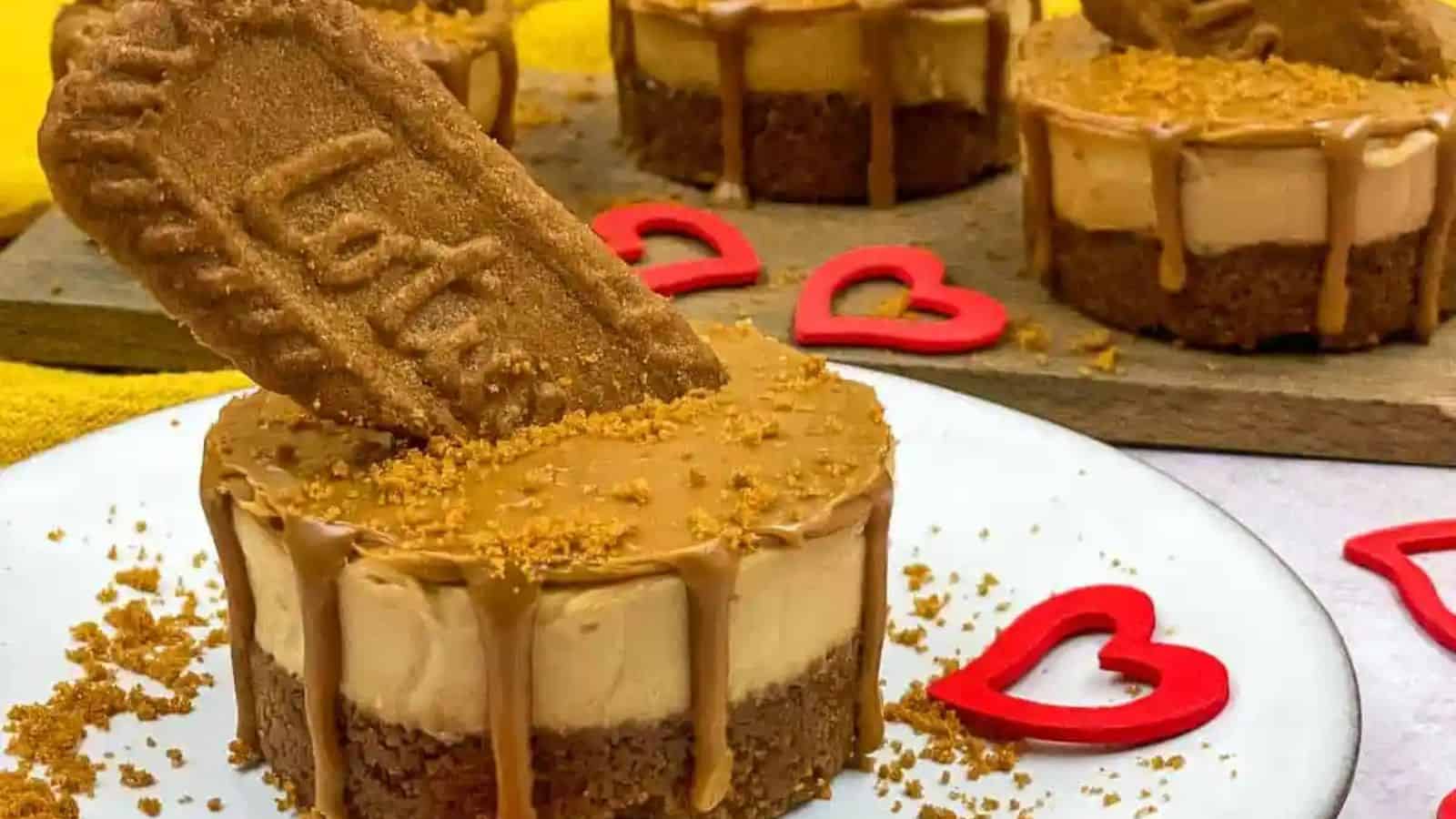 Mini Lotta Biscoff cheesecakes topped with a Biscoff biscuit and caramel drizzle, surrounded by red heart shapes.