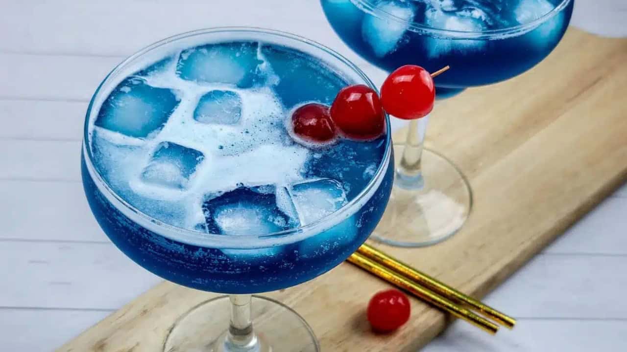 Two blue ocean water cocktails garnished with cherries.
