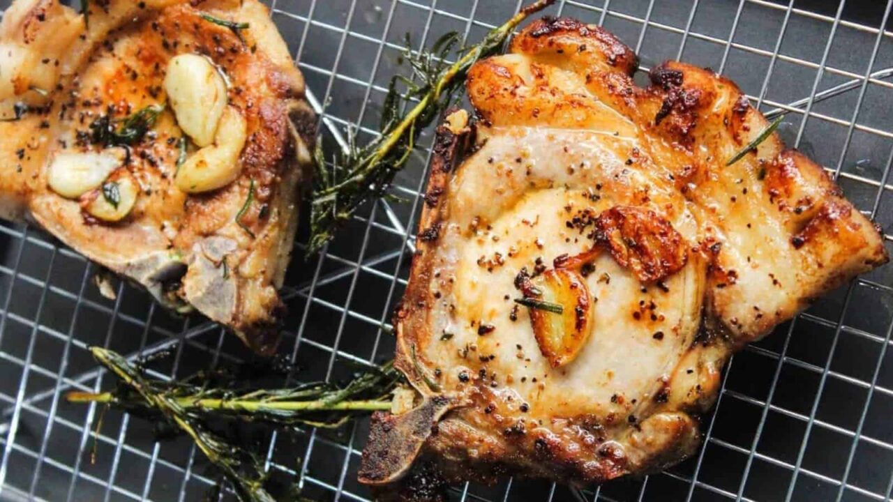 Grilled pork chops with garlic and herbs on a wire rack.