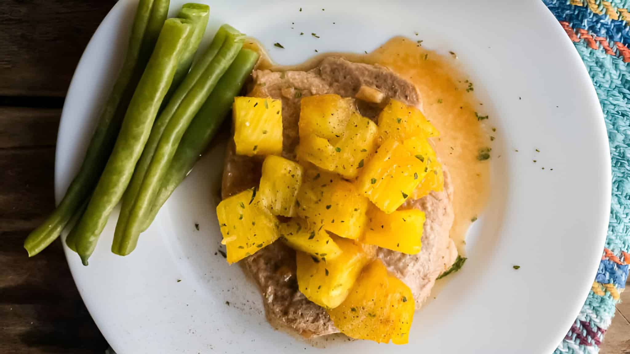 Plate with green beans and a meat patty topped with pineapple chunks and sauce on a white dish.