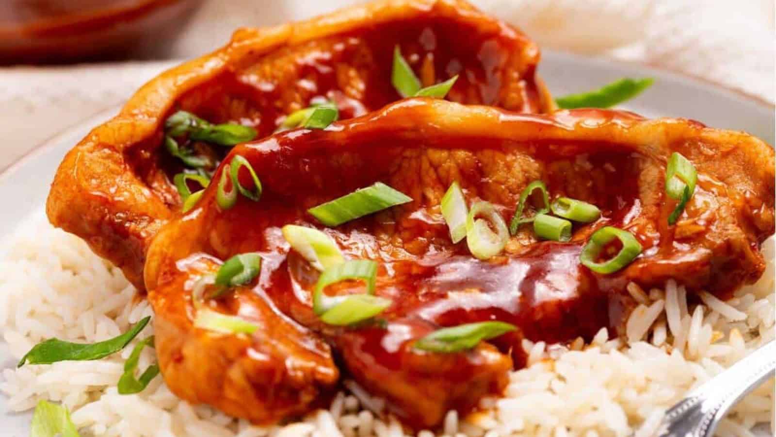 Pork chops topped with sauce and sliced green onions served on a bed of white rice.