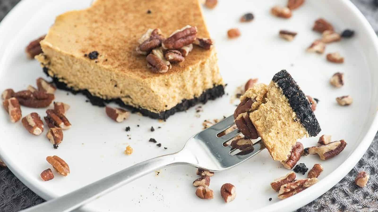A piece of pie with a crumbly base on a white plate, garnished with pecans. A fork holds a small bite of the pie.