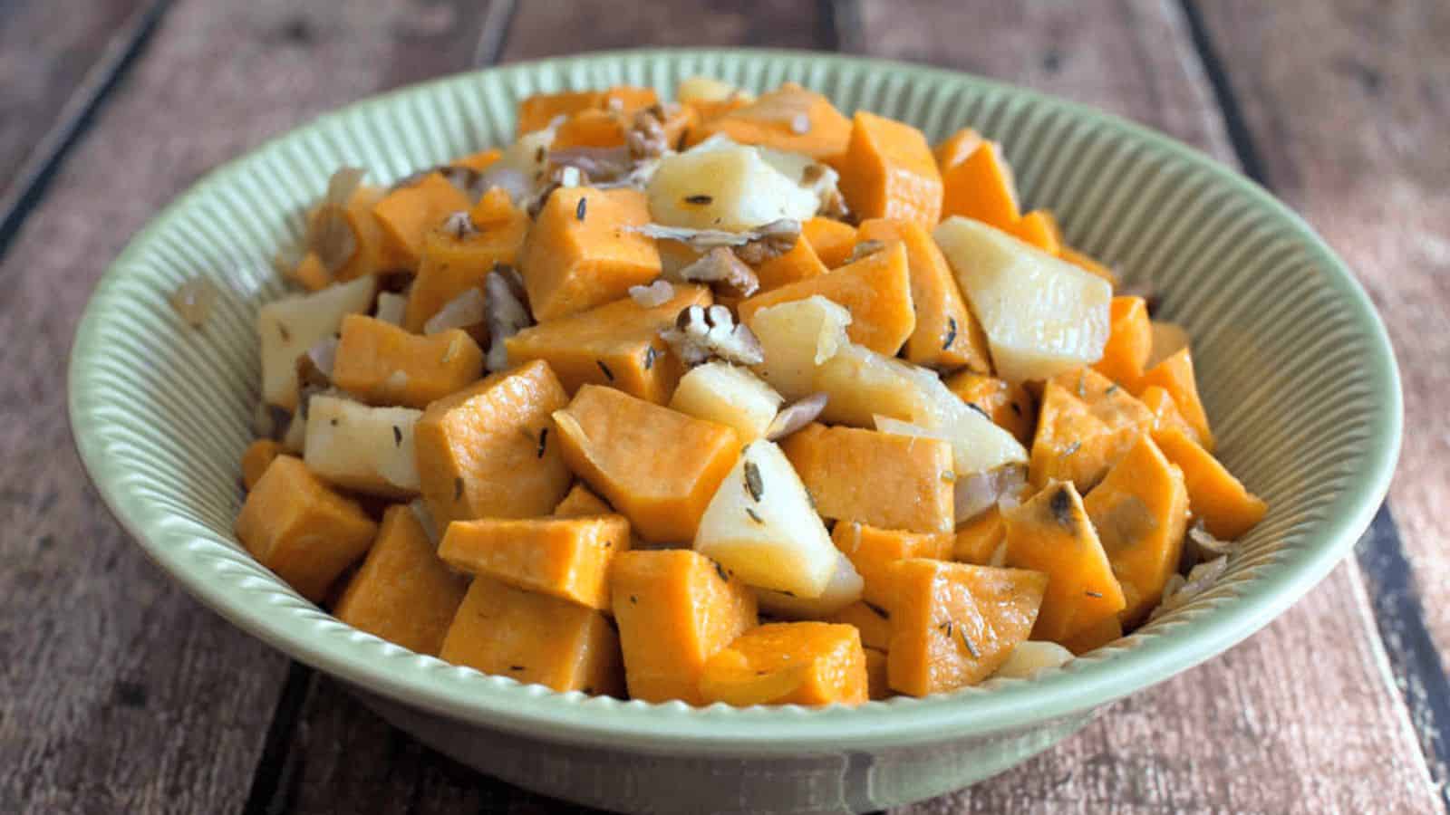 A bowl of diced sweet potatoes and potatoes garnished with herbs on a wooden table.