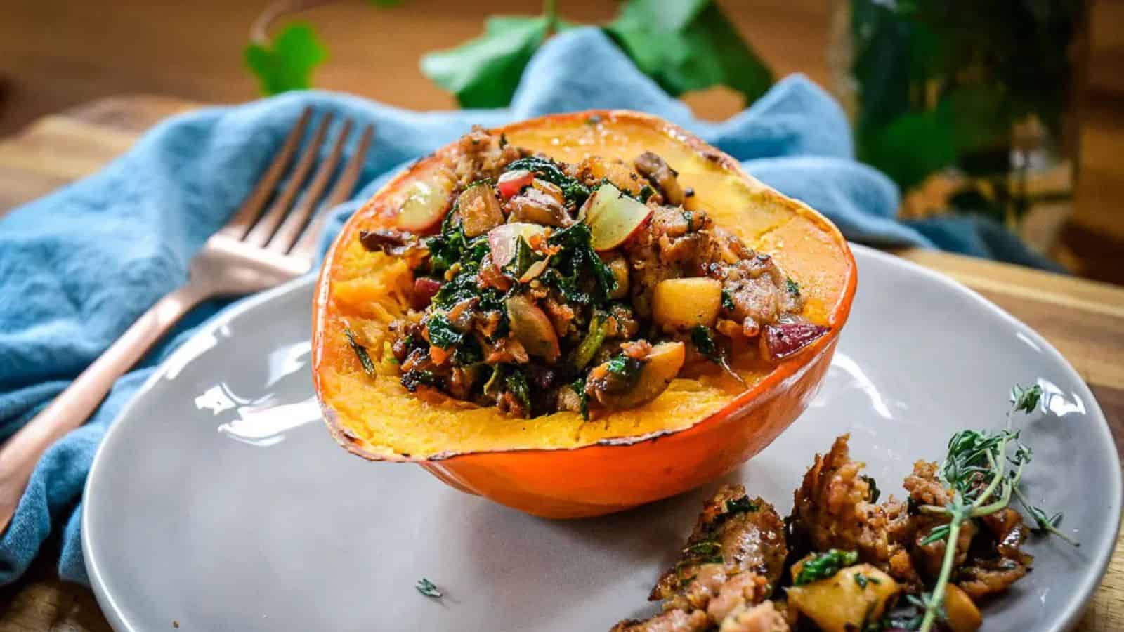 A halved acorn squash stuffed with a mixture of vegetables and herbs on a gray plate, with a fork on a blue cloth in the background.
