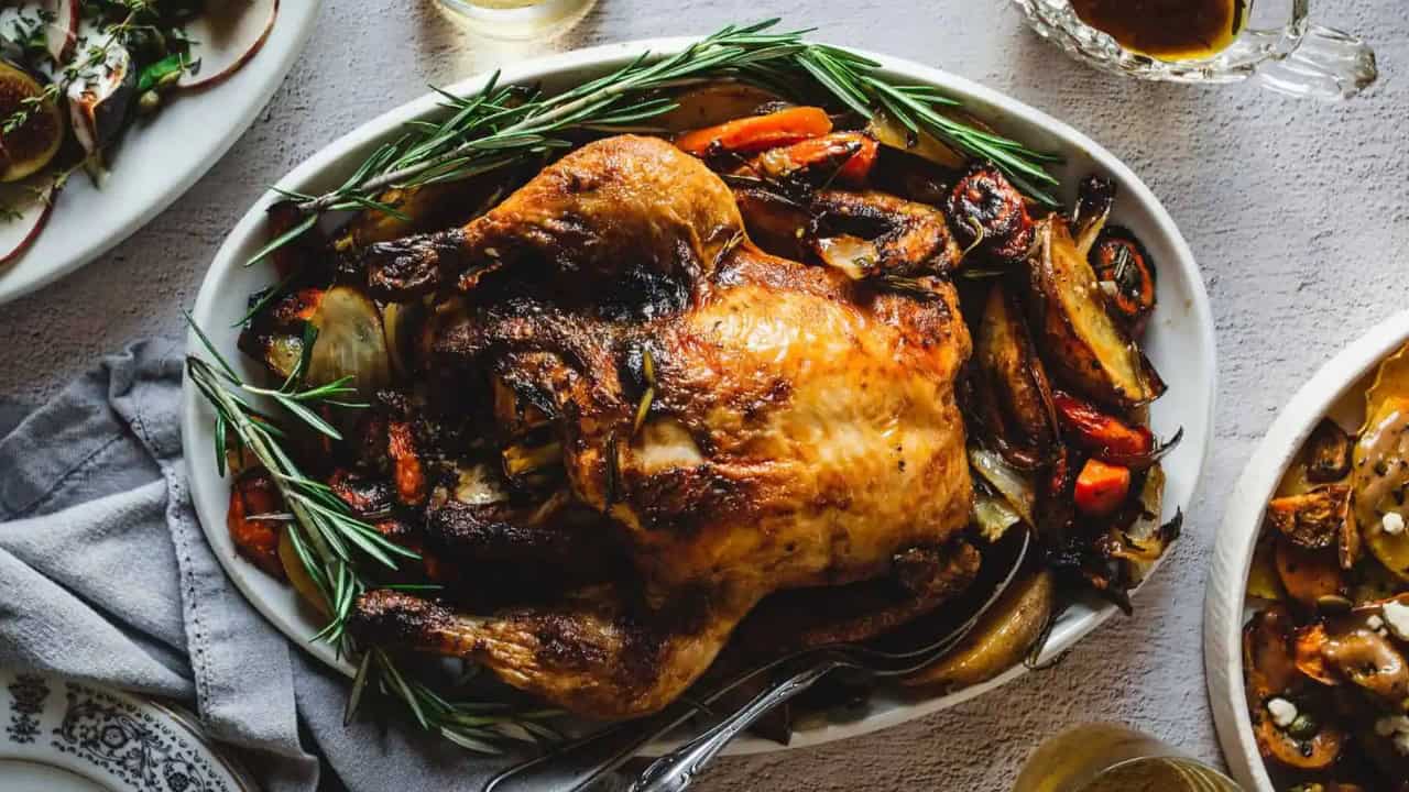 Hands holding paprika chicken and vegetables on a sheet pan.