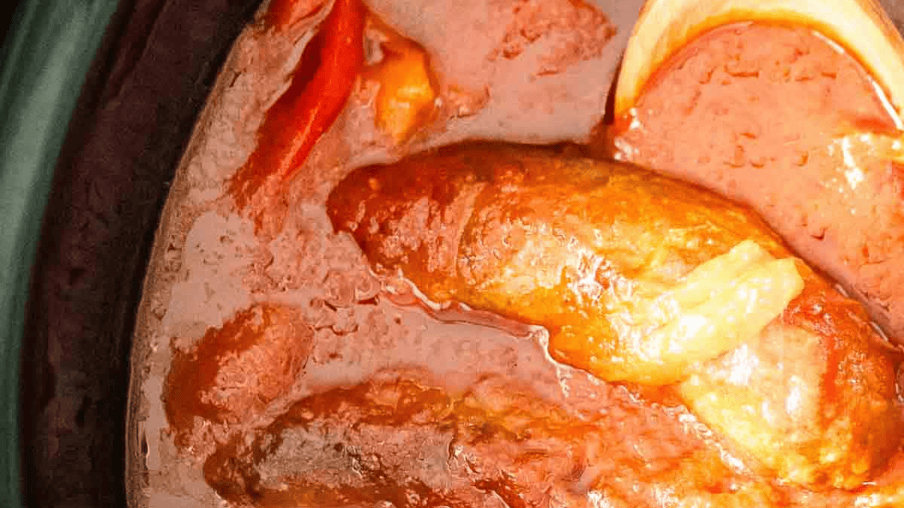 A crock pot full of sausage, peppers, and marinara sauce.