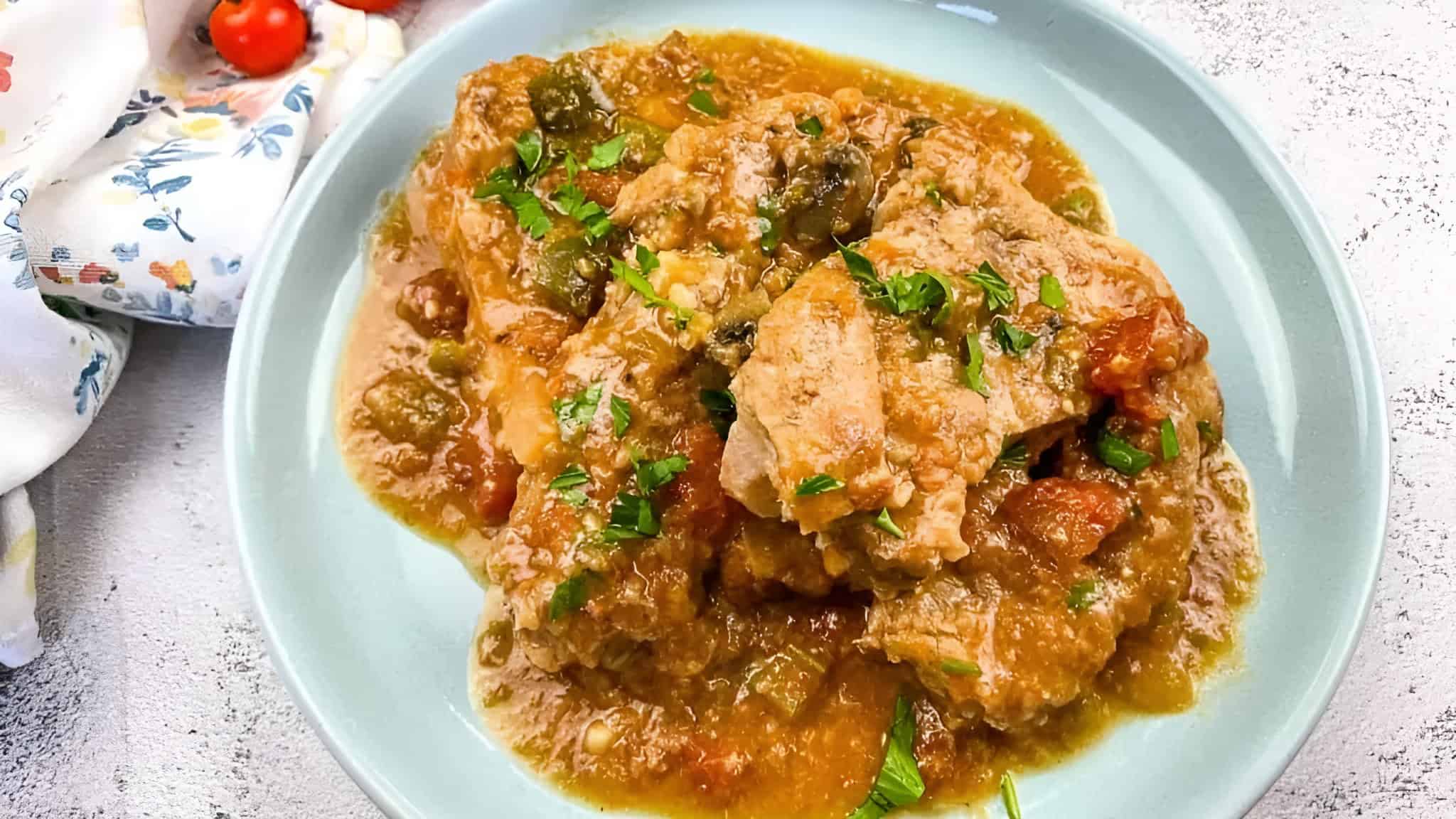 A plate of chicken stew with a tomato-based sauce, garnished with chopped parsley.
