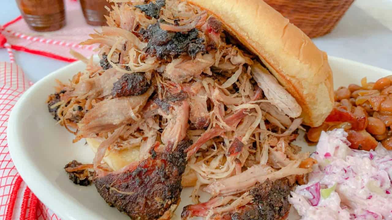 Pulled pork sandwich on a white plate with coleslaw and baked beans on the side.