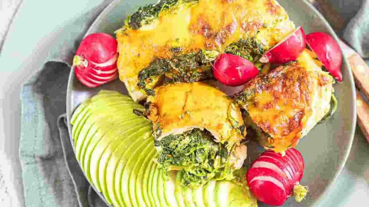 A plate with sliced avocado, radishes, and baked chicken topped with cheese and spinach.