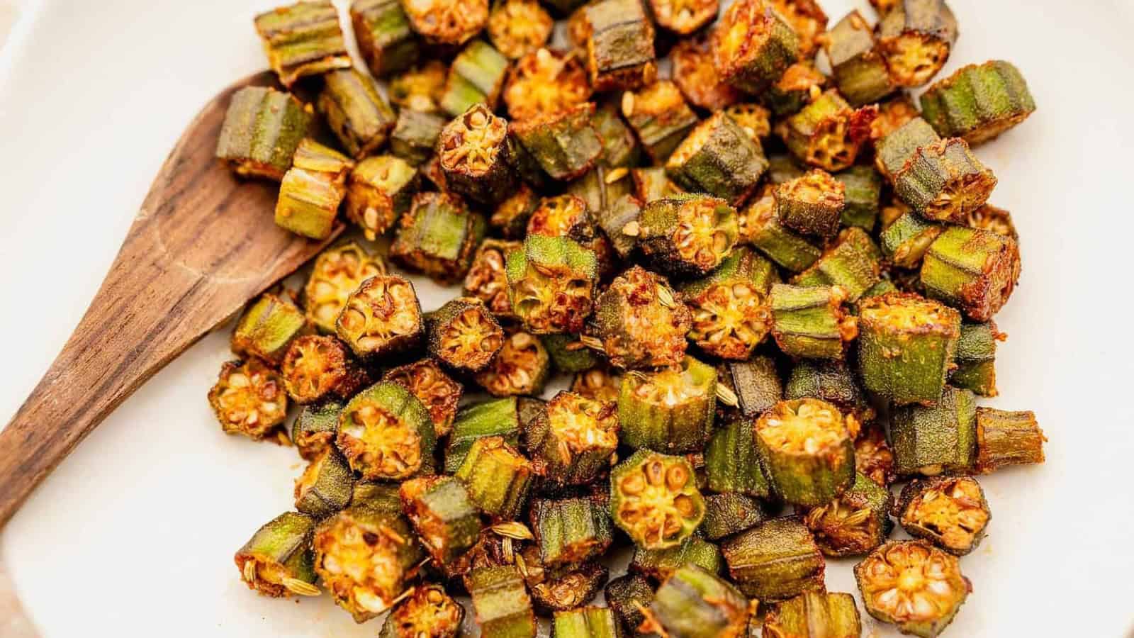A wooden spoon with a pile of sliced, roasted okra on a white surface.