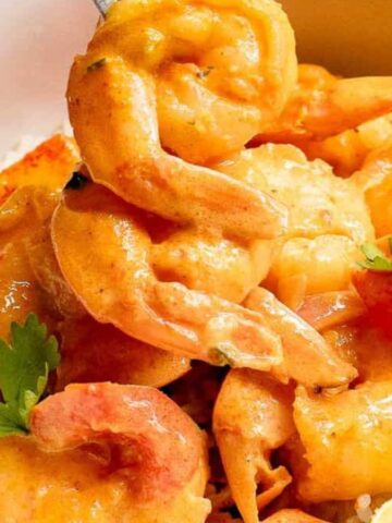 A bowl of rice topped with creamy shrimp curry, garnished with cilantro and lime slices.