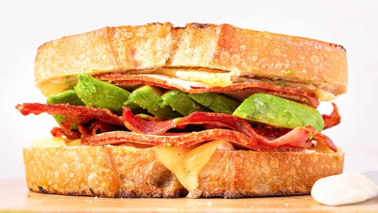A turkey avocado sandwich sits on a red background.