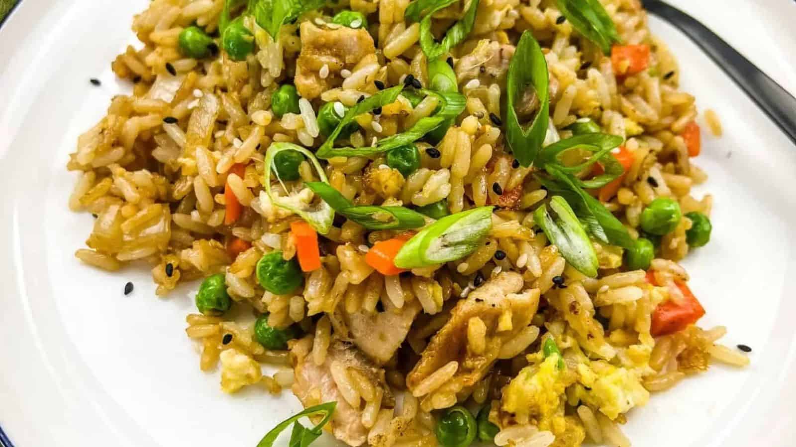 A plate of fried rice with vegetables, sliced green onions, and pieces of chicken.