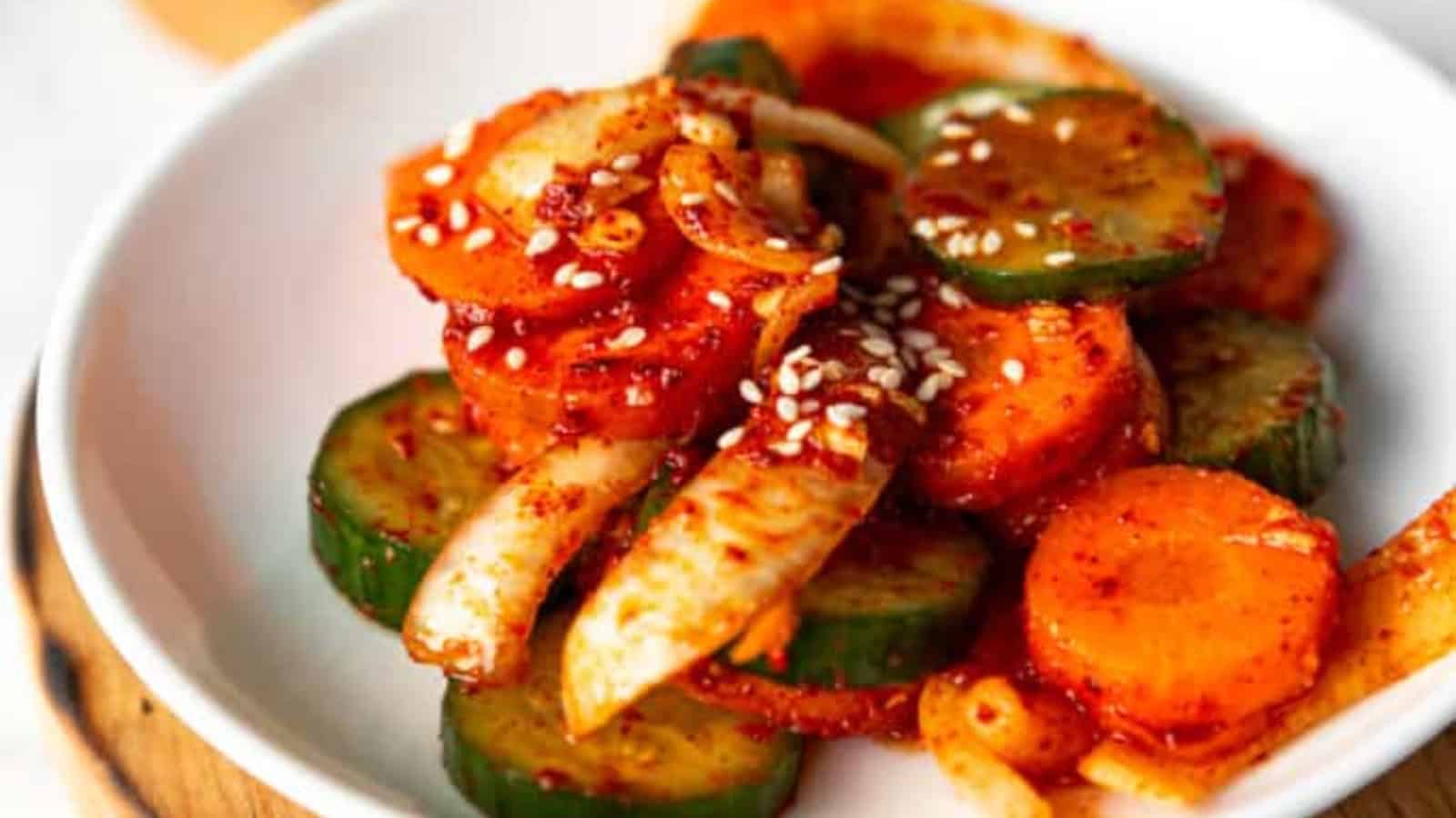 A dish of spicy cucumber and carrot salad with onion, garnished with sesame seeds, on a white plate.