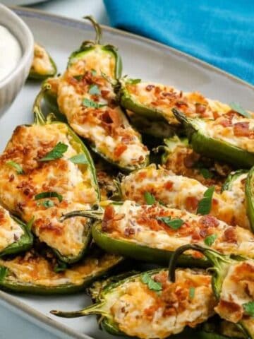 A platter of stuffed jalapeños topped with melted cheese and herbs next to a bowl of white dipping sauce.