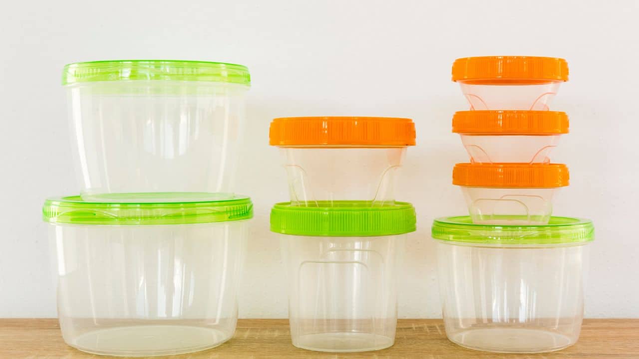 Plastic containers with green and orange lids are stacked on a wooden surface against a white background.