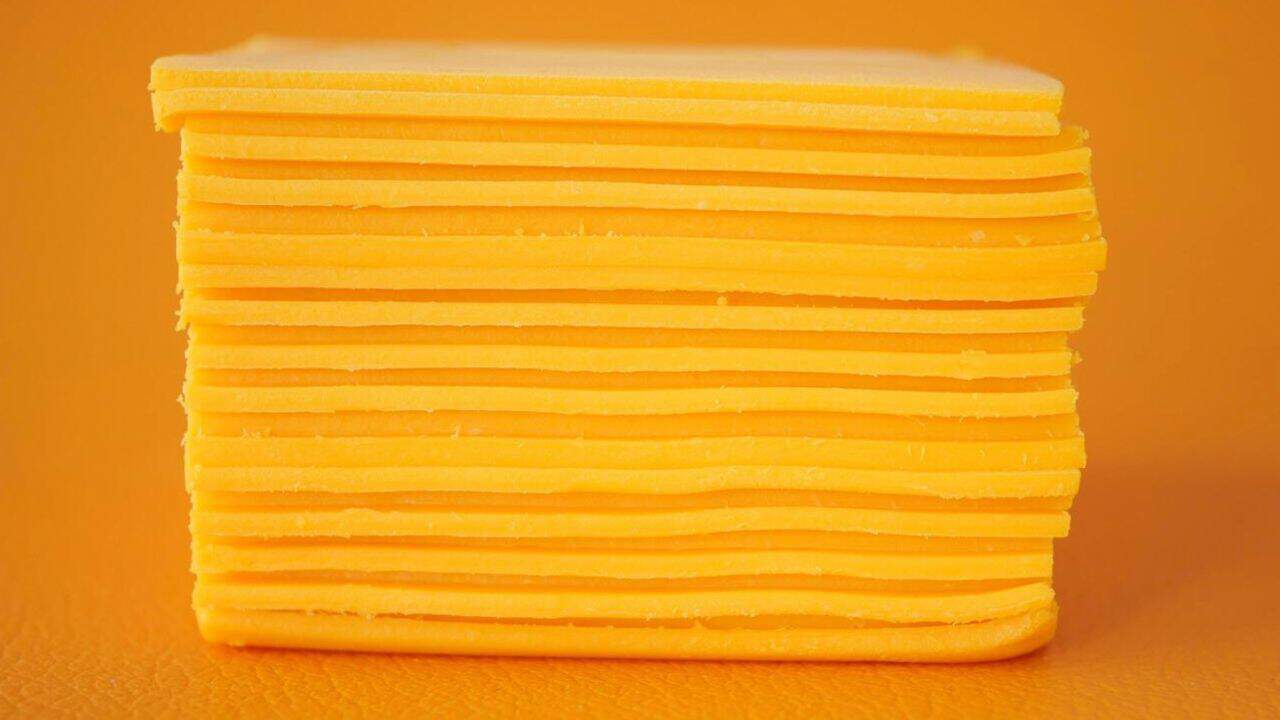 A neat stack of yellow cheese slices against an orange background.
