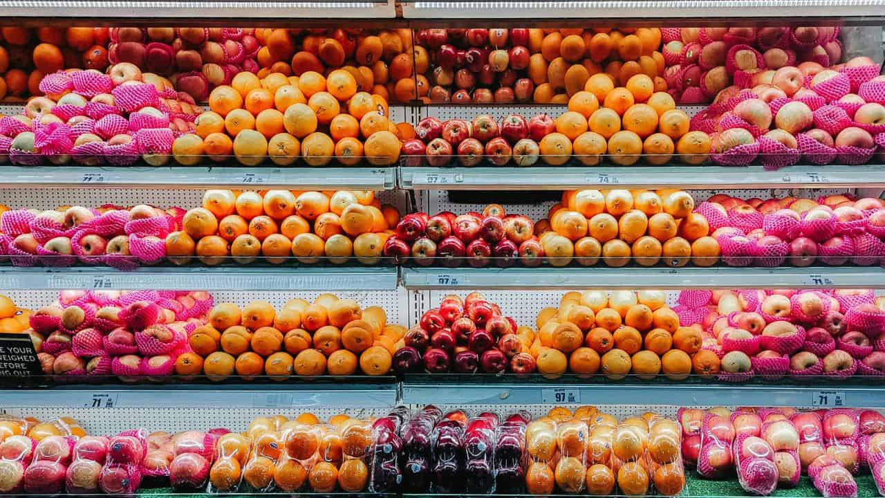 Assorted fruits including apples, oranges, and pomegranates are neatly arranged on shelves in a grocery store.
