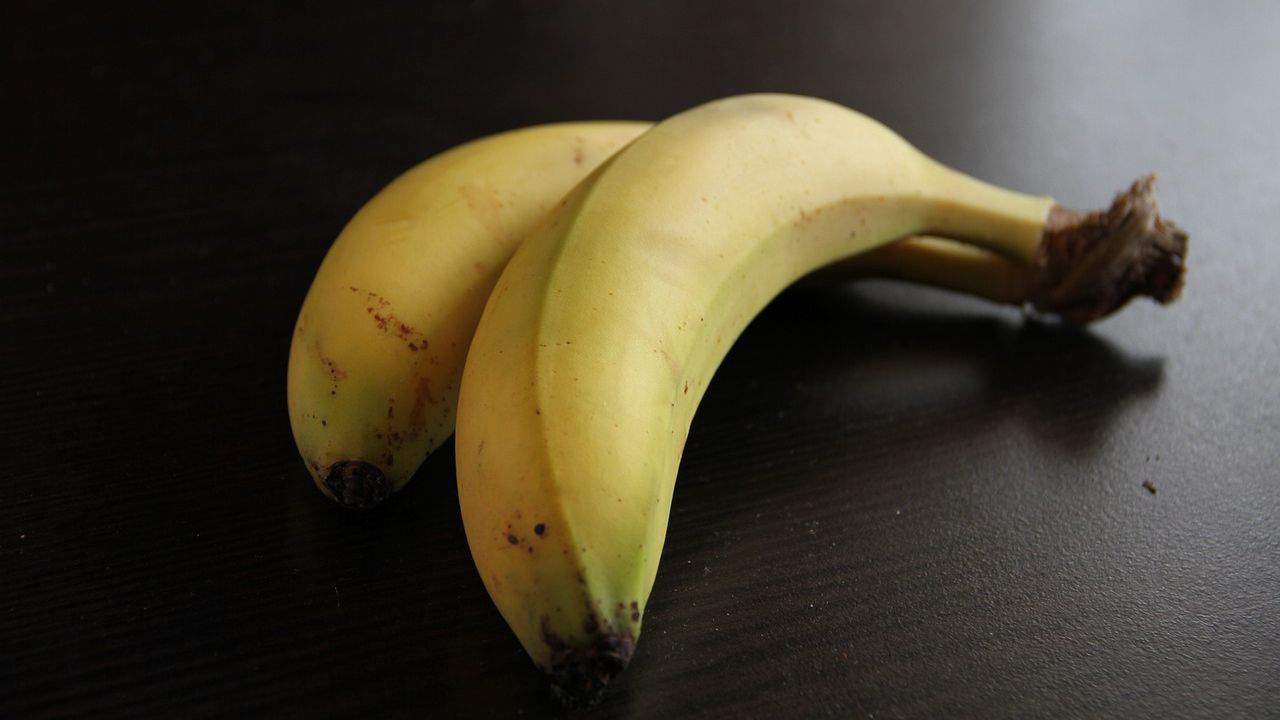 Two ripe bananas lying on a dark surface.