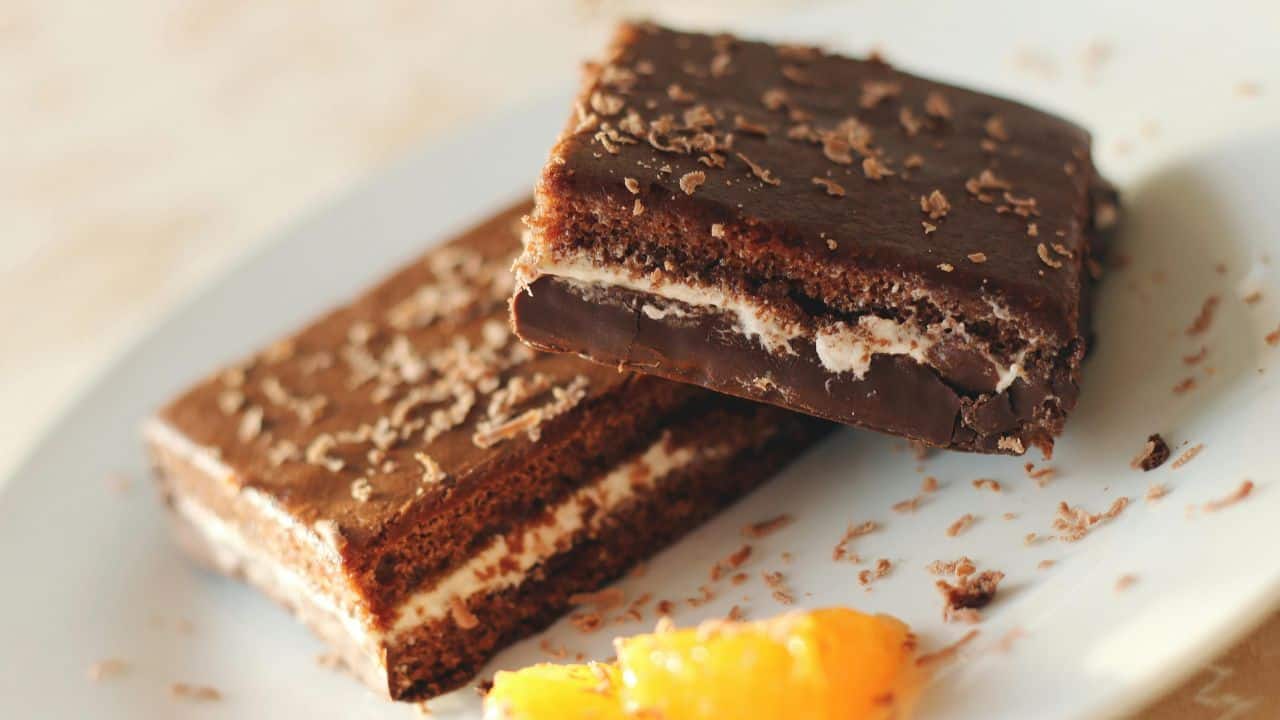 Two chocolate cake slices with cream filling on a plate, garnished with chocolate shavings and a small piece of orange.
