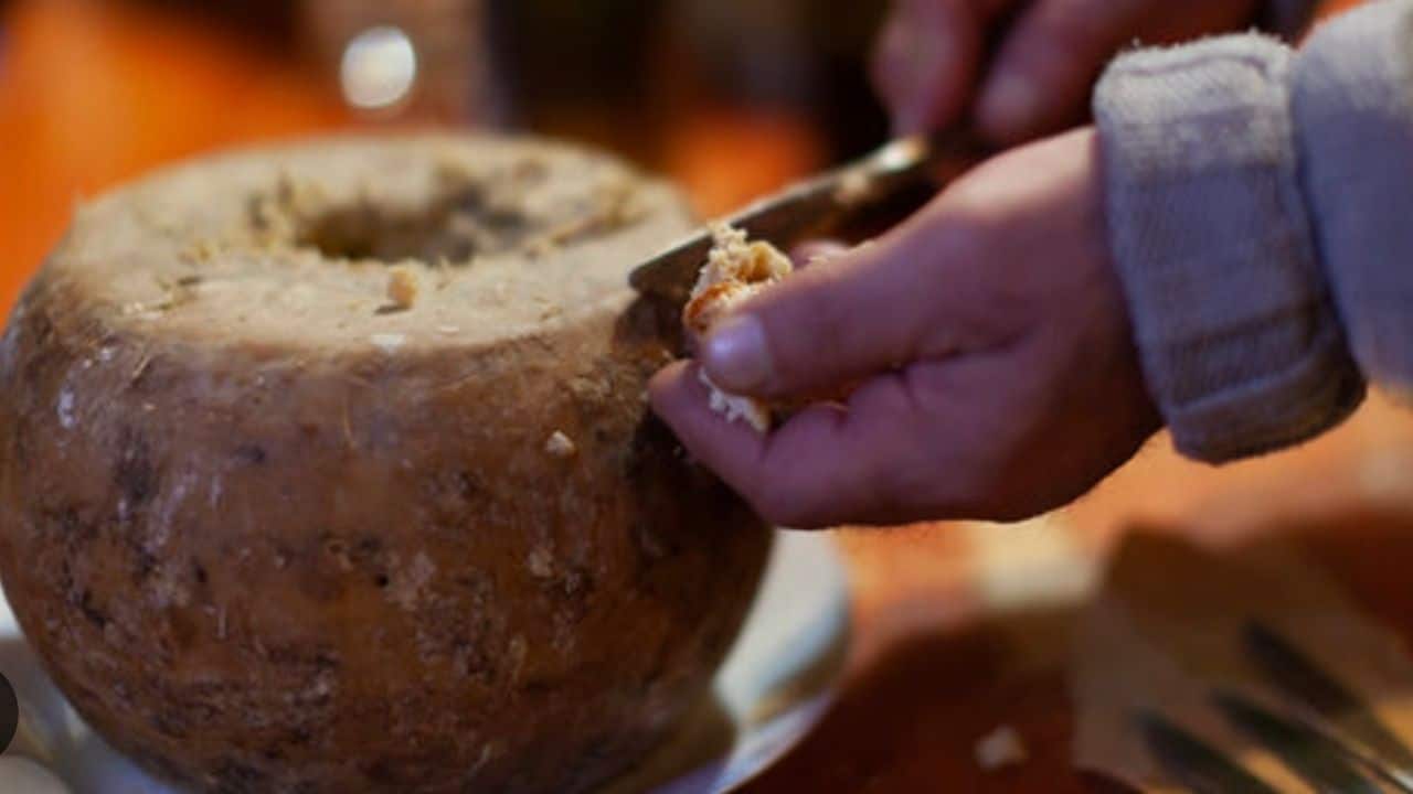 A person slices into a round cheese with a knife.