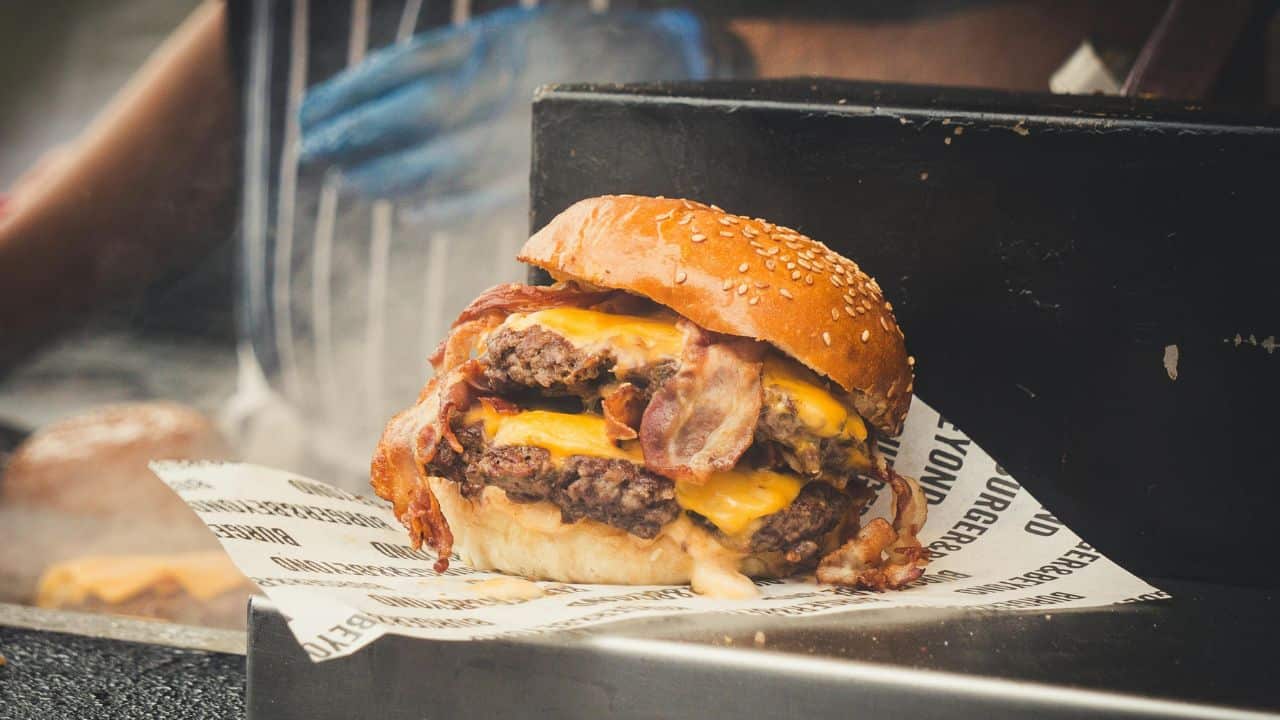 A double cheeseburger with bacon is placed on a sheet of branded paper.