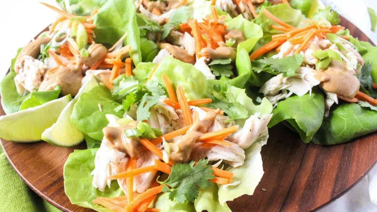 Lettuce wraps filled with shredded chicken, shredded carrots, and peanut sauce on a plate.