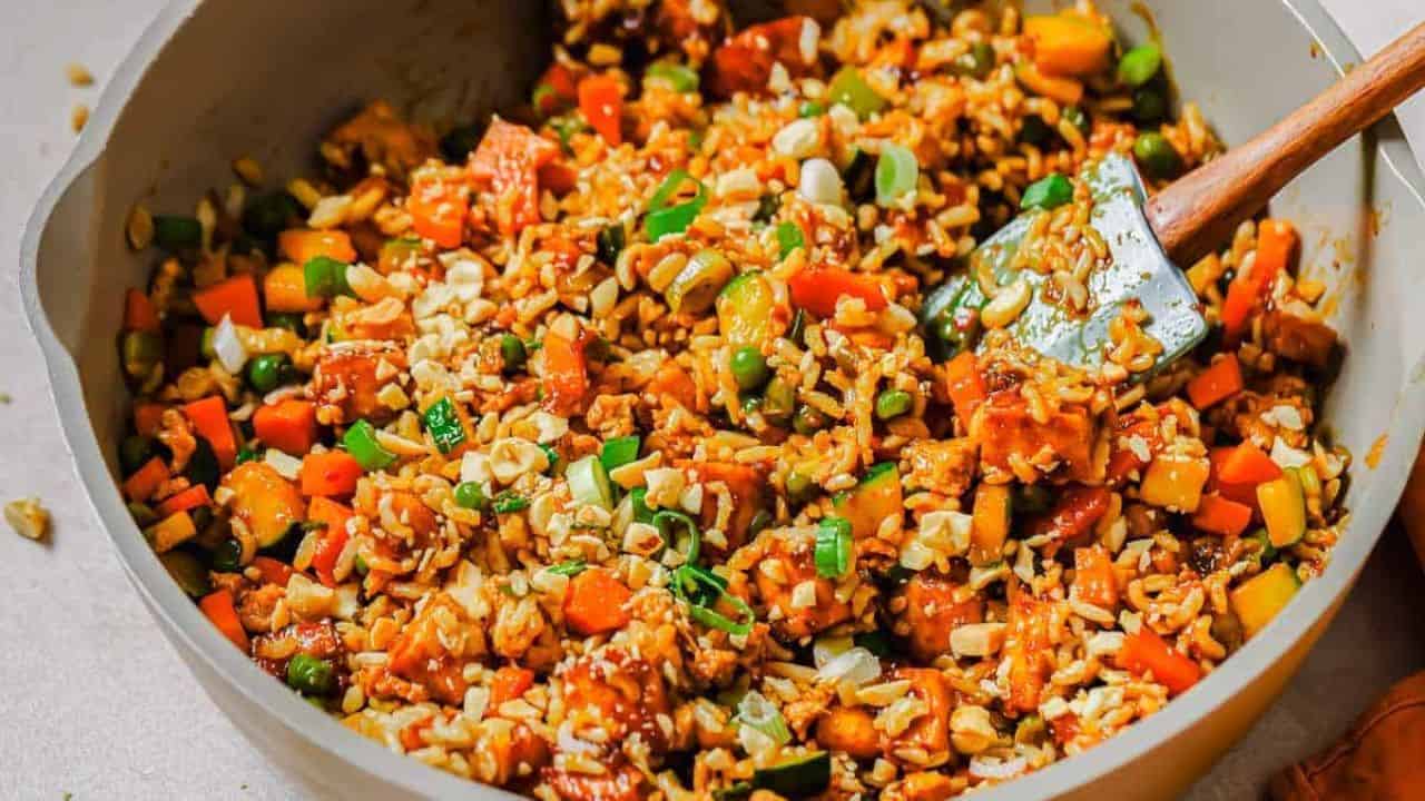 A skillet filled with colorful fried rice, including vegetables and garnished with chopped green onions.