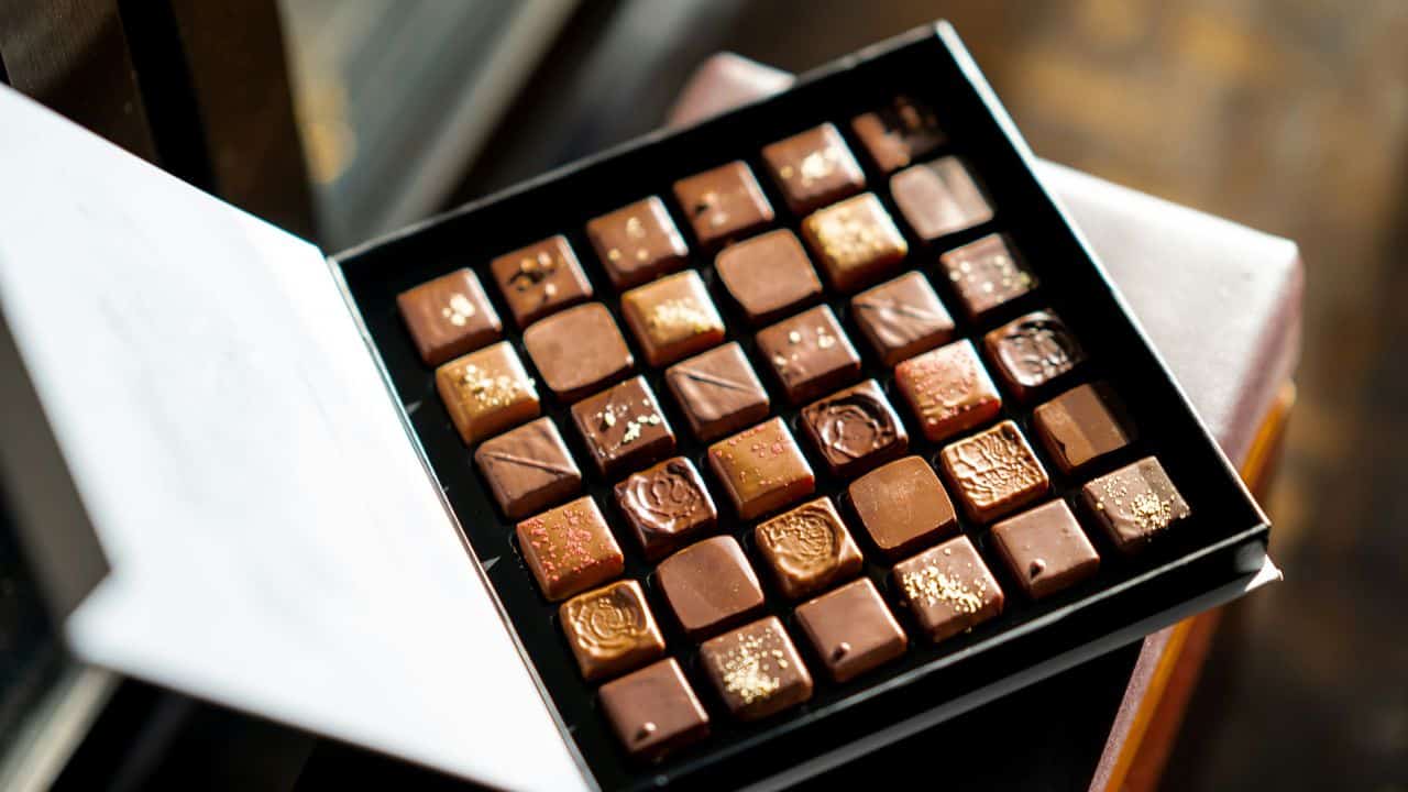 A box of assorted chocolates arranged in rows, featuring various designs and toppings.