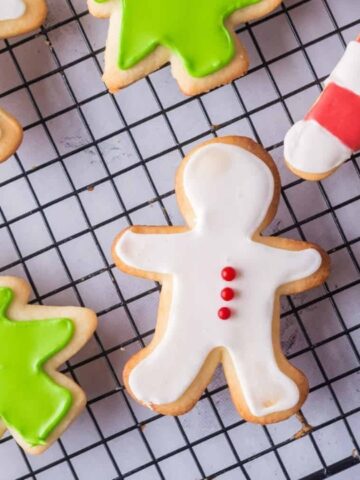 Christmas-themed sugar cookies shaped like trees, candy canes, and gingerbread figures with green, red, and white icing, placed on a wire cooling rack.