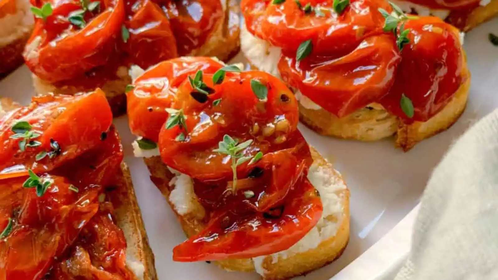 Toast topped with roasted tomatoes, fresh thyme, and melted cheese on a plate.