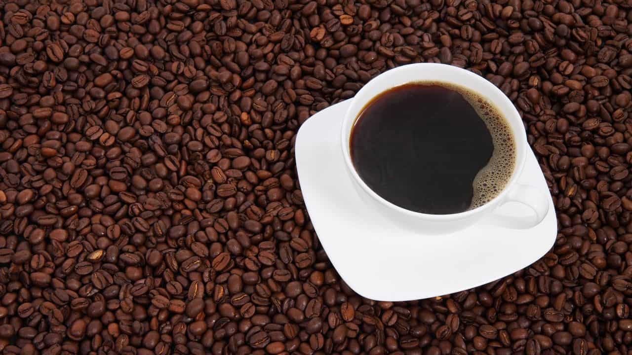 A cup of black coffee on a saucer sits atop a large pile of roasted coffee beans.