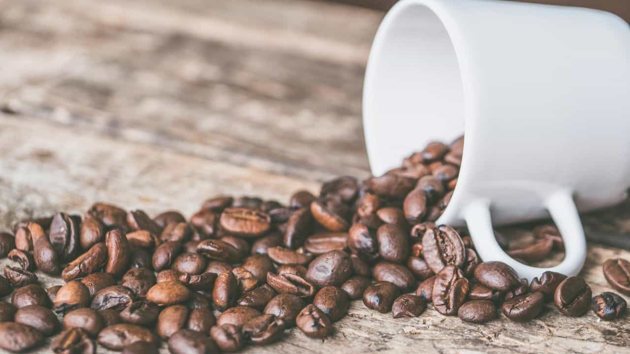 White mug tipped over, spilling coffee beans onto a rustic wooden surface.