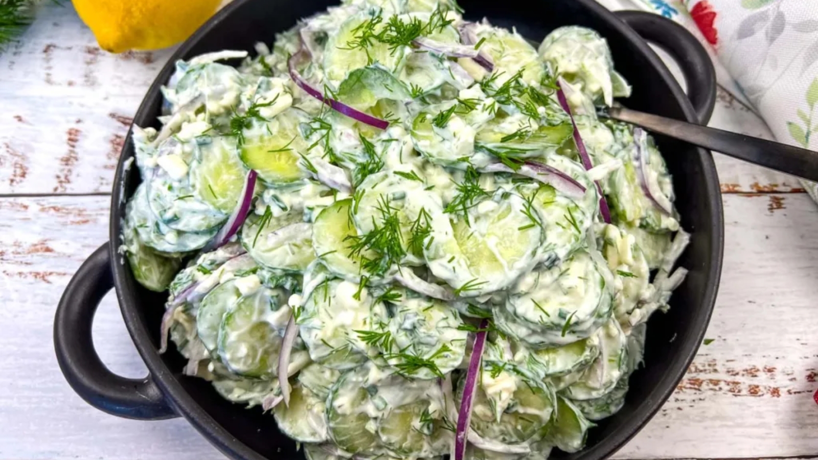 A bowl of creamy cucumber salad topped with red onion slices and fresh dill.