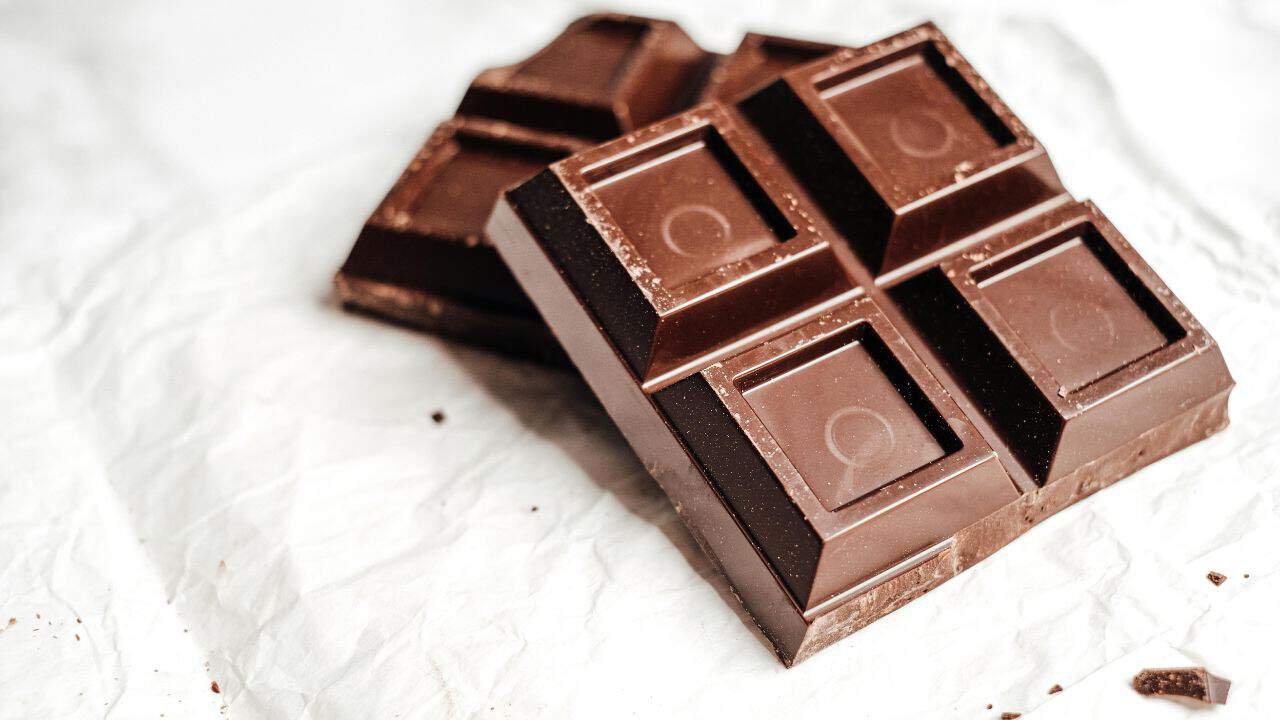 Two pieces of dark chocolate on crumpled white paper, showing square sections and slight surface texture.