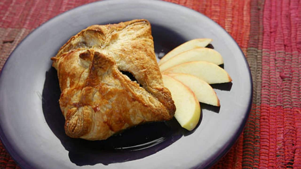 A puff pastry on a blue plate is served with three slices of apple on a red woven placemat.