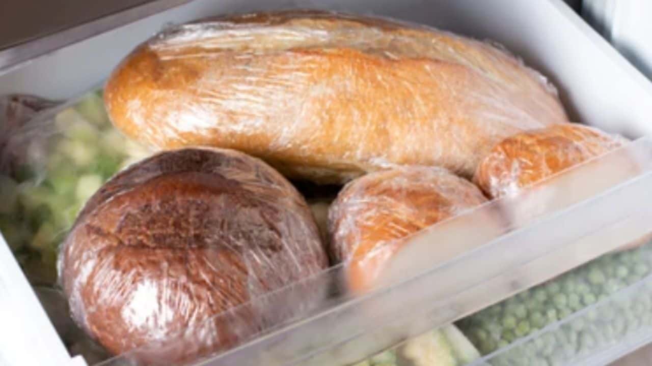 Bread loaves wrapped in plastic sitting inside a freezer drawer with bags of frozen vegetables.