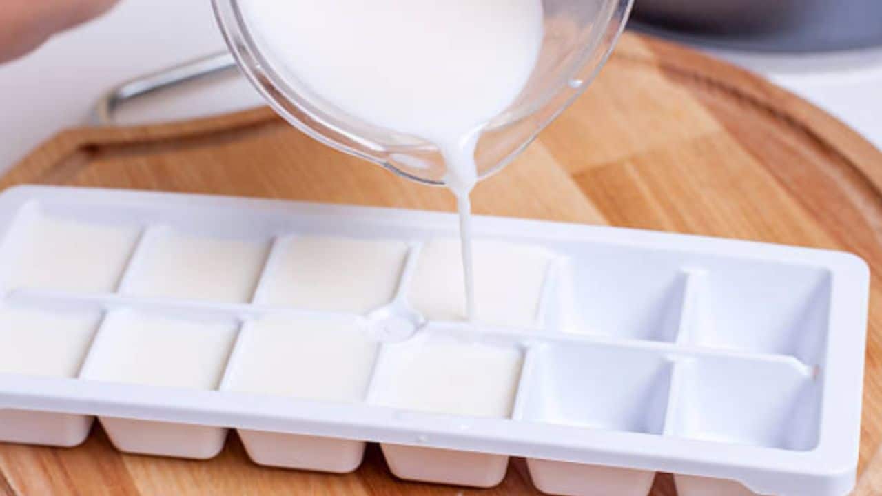 Milk being poured into an ice cube tray on a wooden surface.