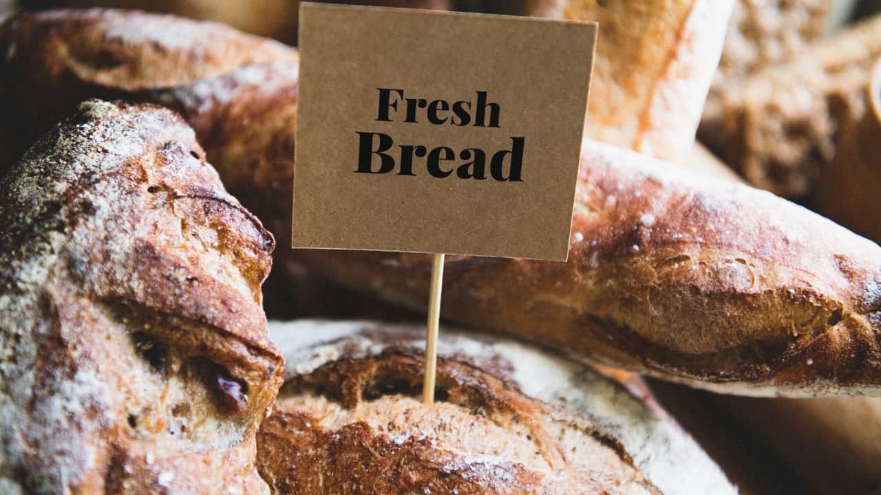 A sign labeled "Fresh Bread" is placed among several loaves of crusty bread.