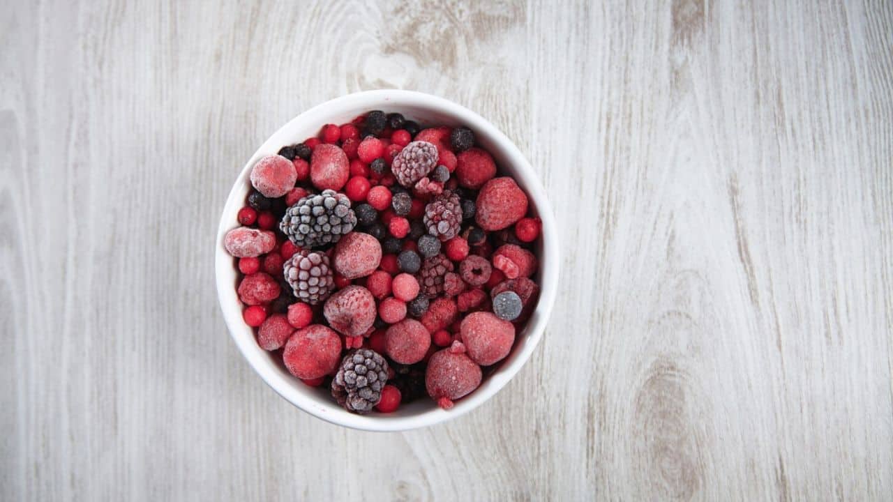 A bowl filled with a variety of frozen berries on a wooden surface.