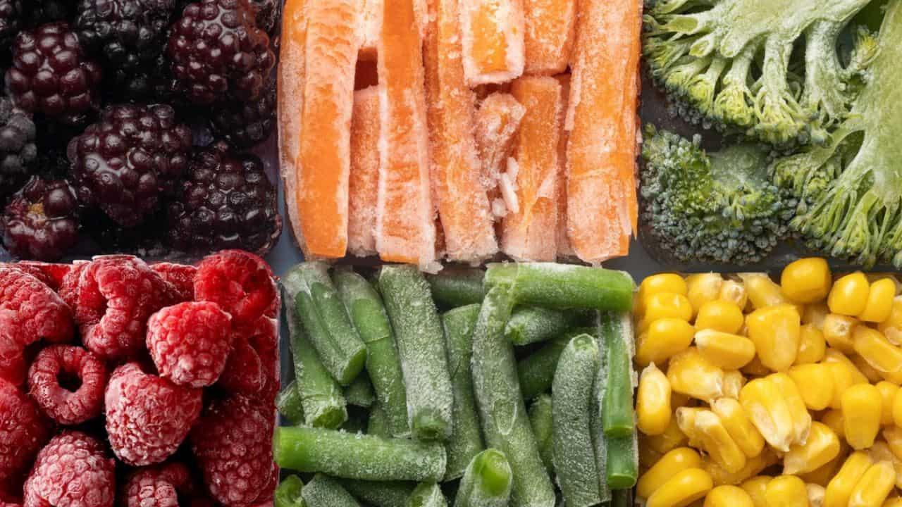 A variety of frozen vegetables and berries arranged in a grid: blackberries, raspberries, carrot sticks, green beans, broccoli, and corn.