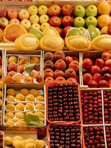 A colorful assortment of fruits, including apples, cherries, papayas, and pears, displayed in neat rows at a market.